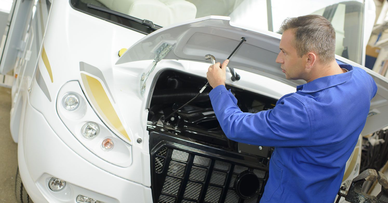 Mechaniker steht vor Wohnmobil im Service mit offener Motorhaube